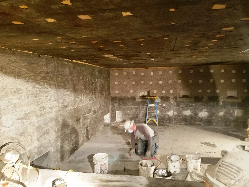 Construction workers stand in a large Aluminum melt furnace, relining the furnace.